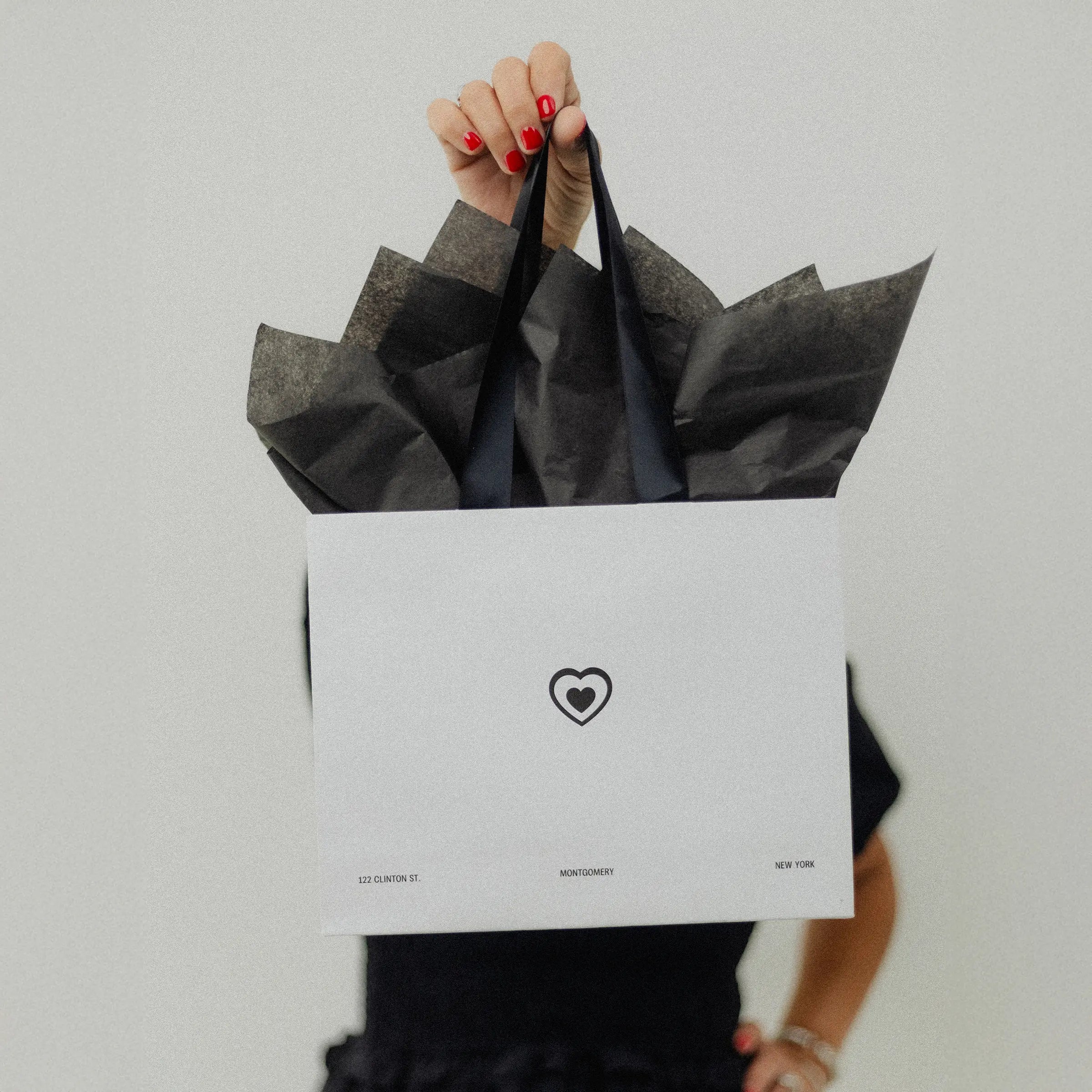 Person holding a black gift bag with a white label featuring a heart symbol.