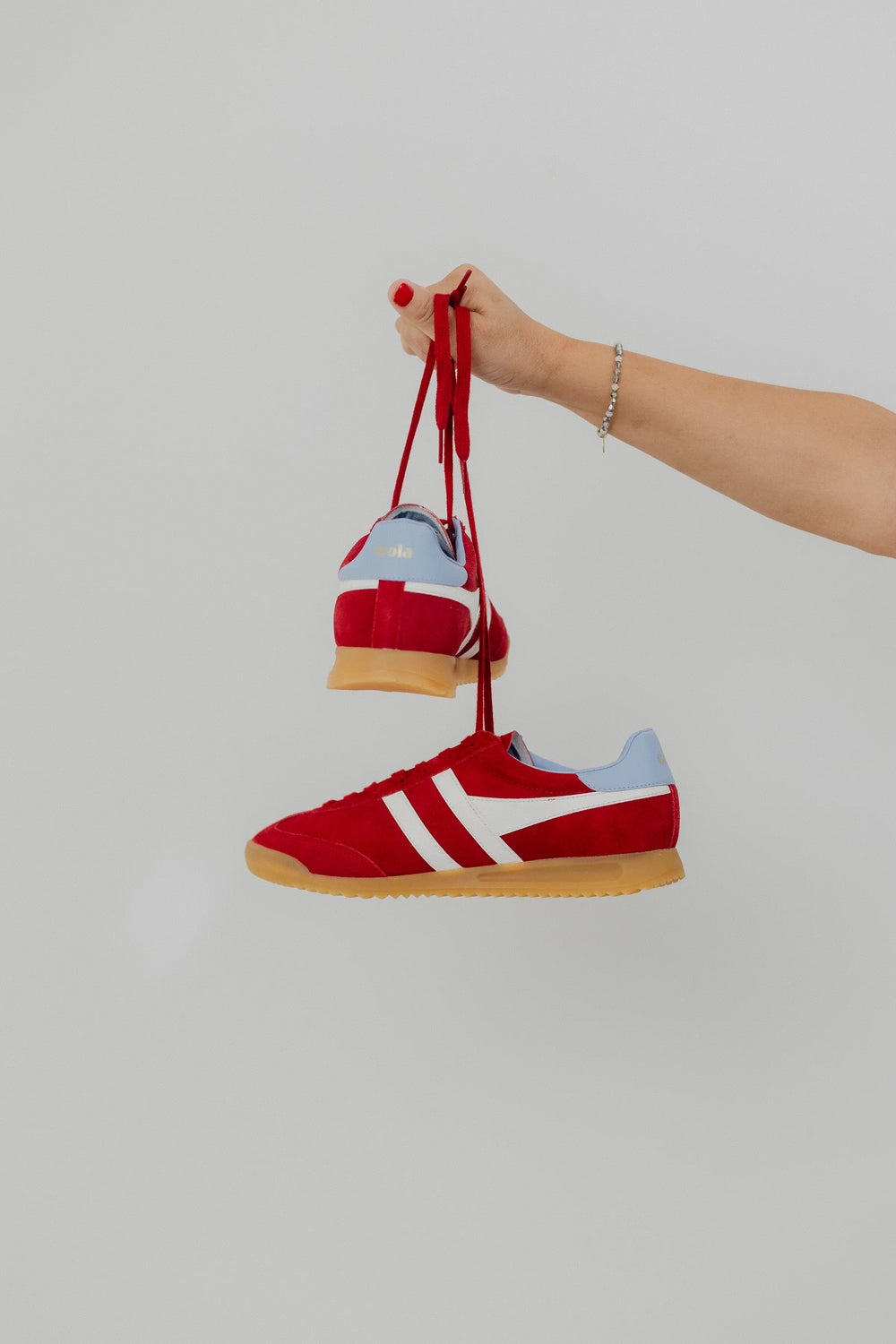 Red sneakers with white logo held by a hand against a light gray background