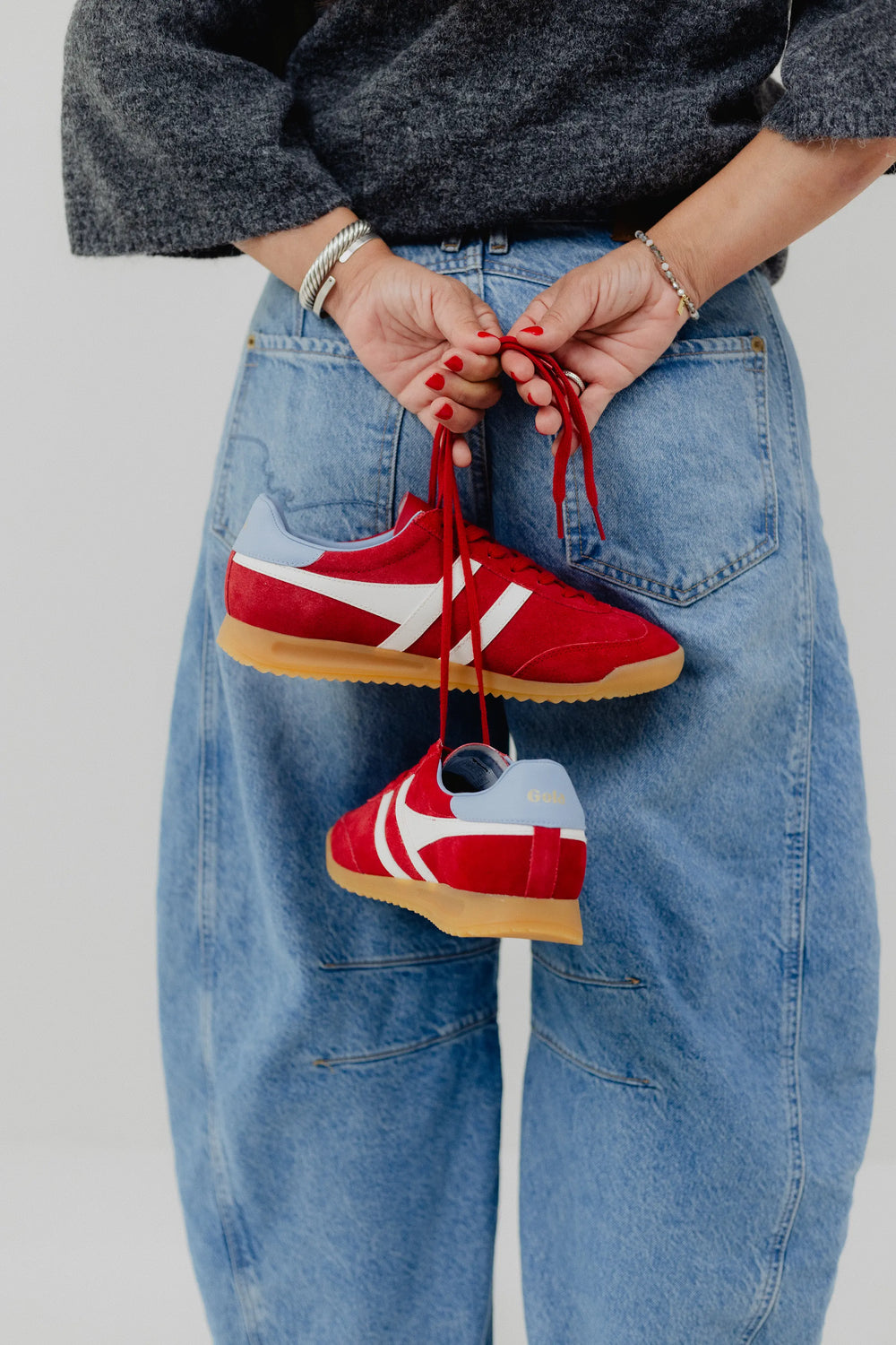 Red sneakers with white logo held by a hand against a light gray background