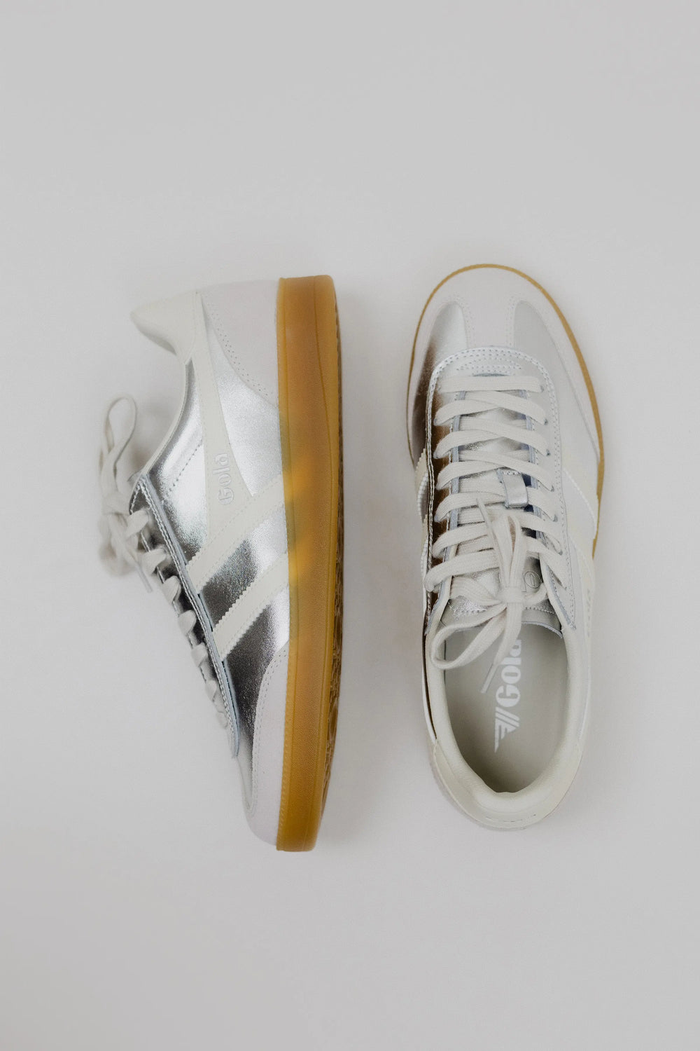 Pair of white sneakers with brown soles on a light gray background