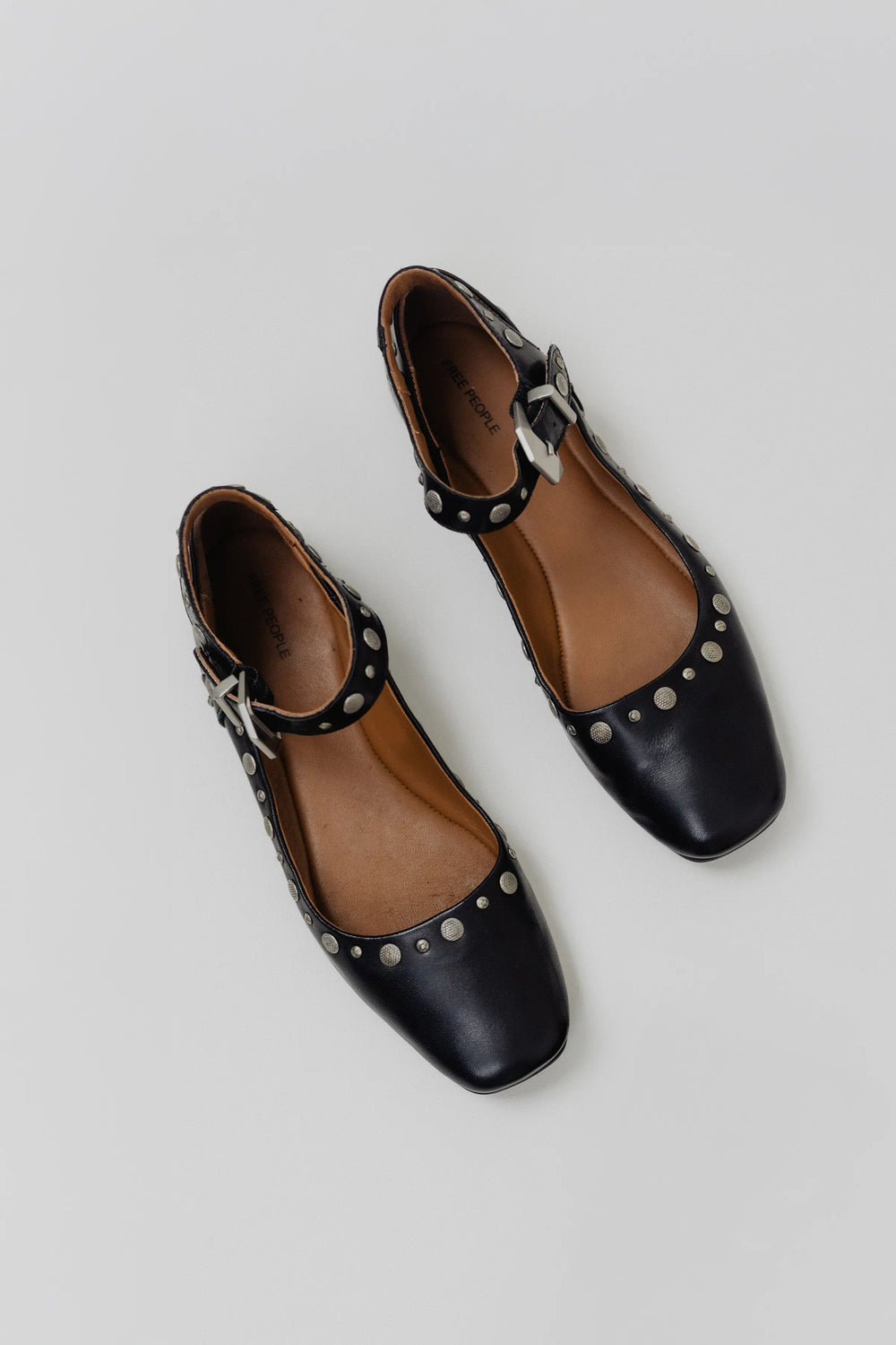 Black flat shoes with studded details on a light gray background