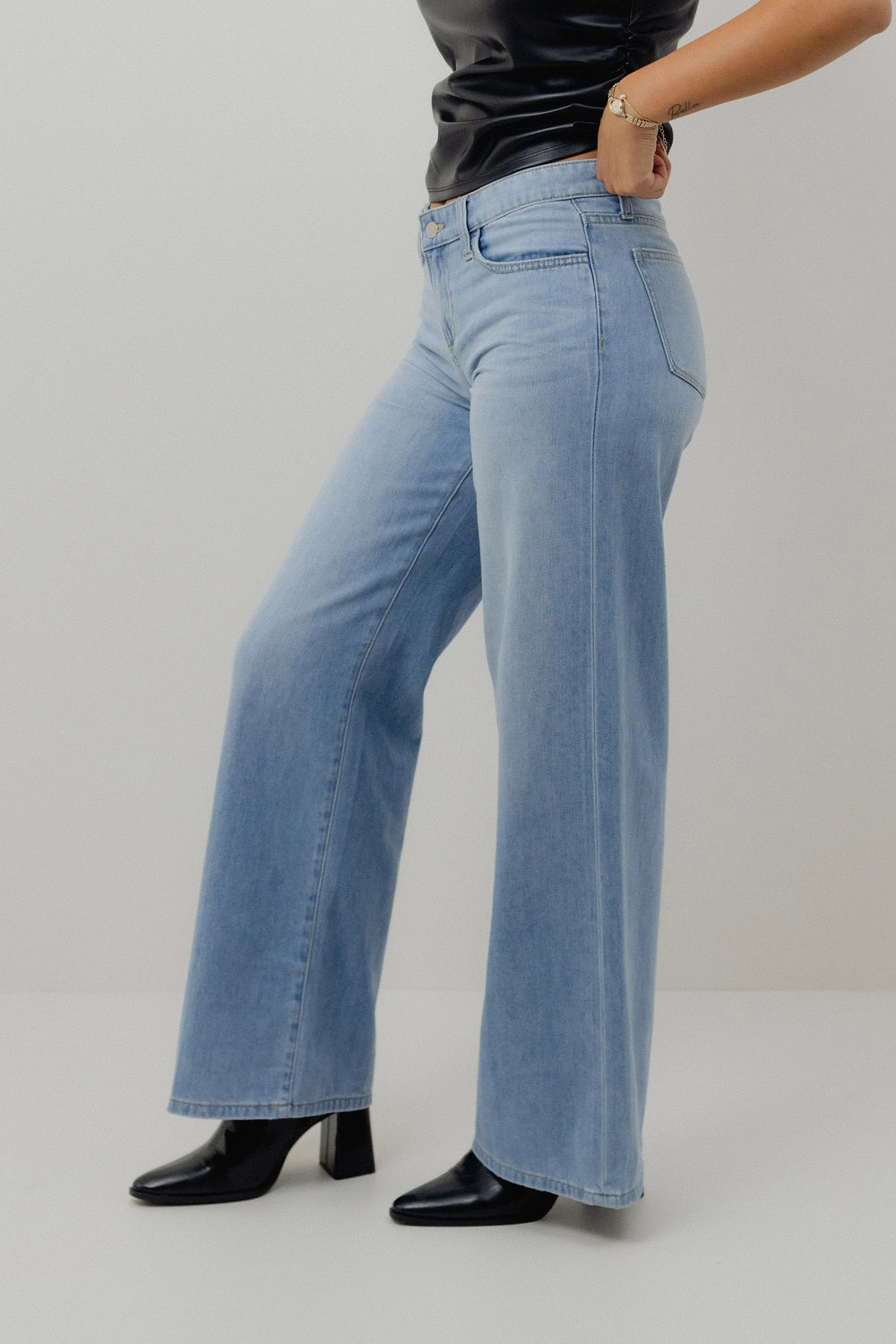 Person wearing light blue jeans and black shoes on a plain background