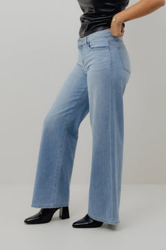 Person wearing light blue jeans and black shoes on a plain background