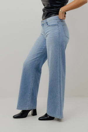 Person wearing light blue jeans and black shoes on a plain background