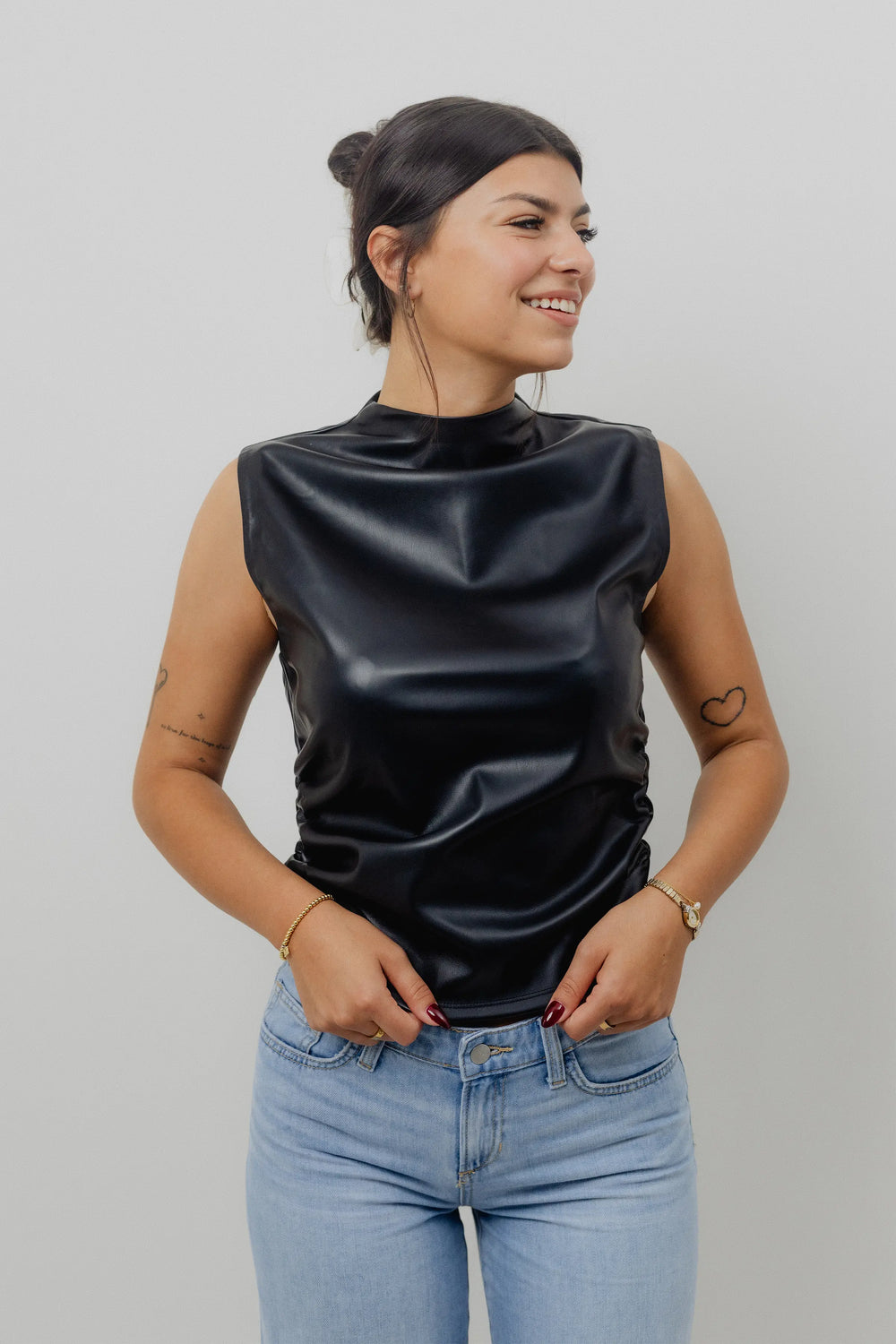 Woman wearing a black sleeveless top and blue jeans against a plain background