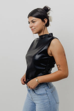 Woman wearing a black sleeveless top and light blue jeans against a plain background