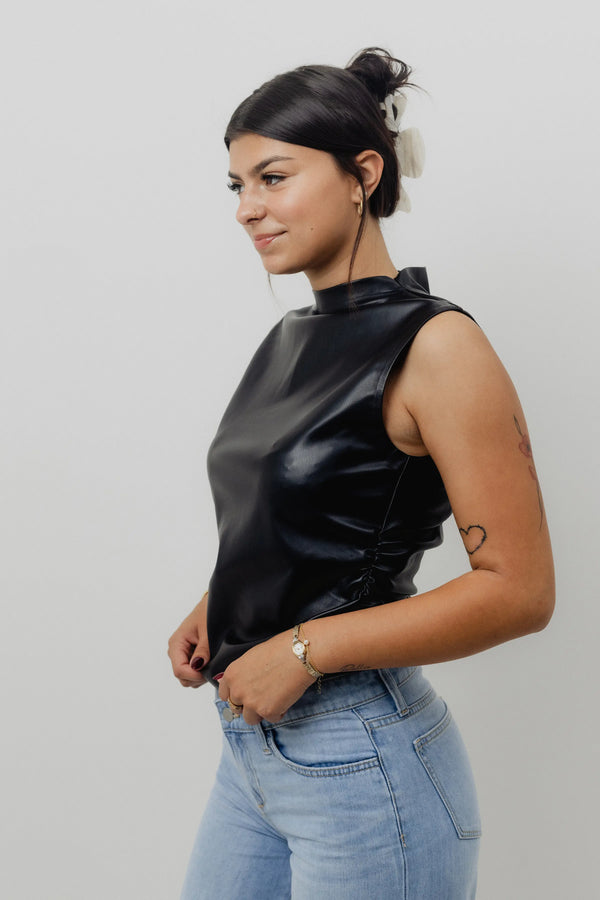 Woman wearing a black sleeveless top and light blue jeans against a plain background