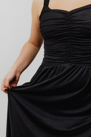 Black dress with ruched bodice and flowing skirt on a plain background