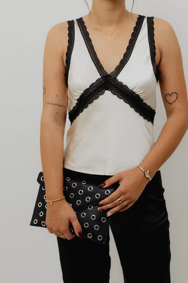 Person wearing a white tank top with black lace details and black pants.