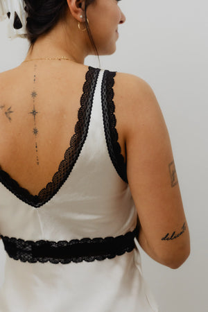 Person wearing a white dress with black lace details on a plain background