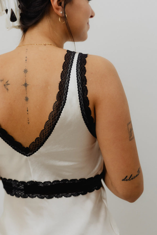 Person wearing a white dress with black lace details on a plain background