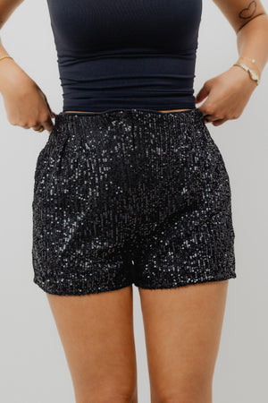 Person wearing black sequin shorts and a dark top on a plain background