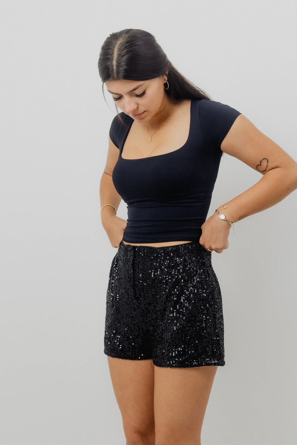 Person wearing black sequin shorts and a dark top on a plain background