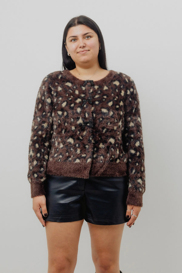 Person wearing a patterned sweater and black shorts against a plain background