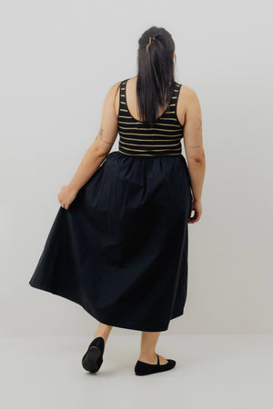 Person wearing a black dress with a striped top on a plain background