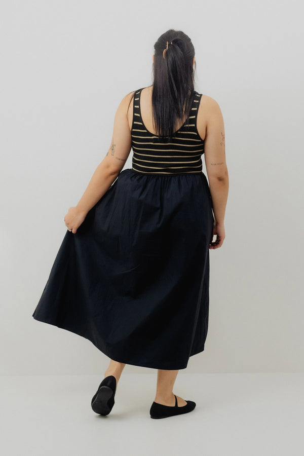 Person wearing a black dress with a striped top on a plain background