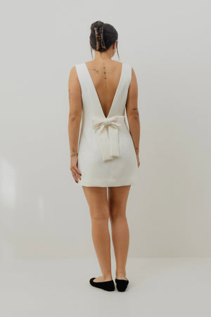Woman wearing a white dress with a deep back bow on a plain background