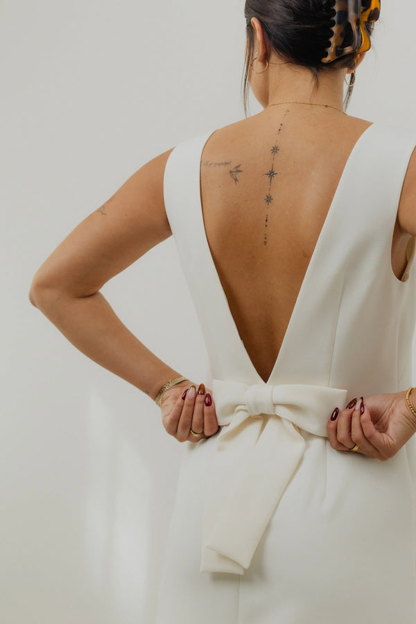 Woman wearing a white dress with a deep backless design, standing against a neutral background.
