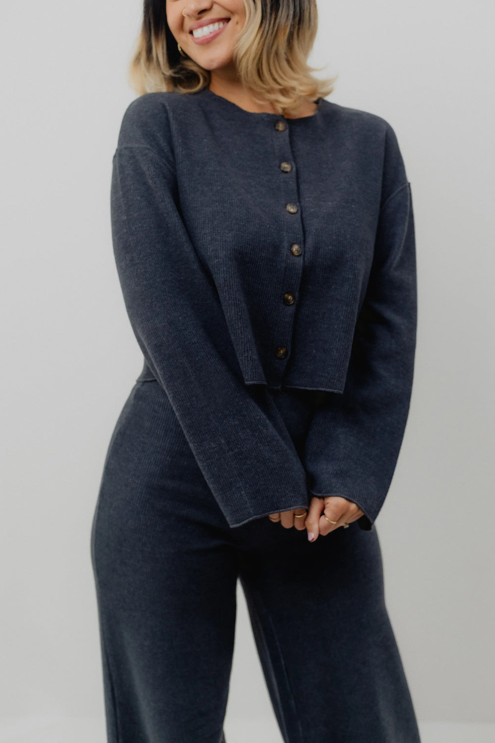 Person wearing a dark gray cardigan with button details on a plain background