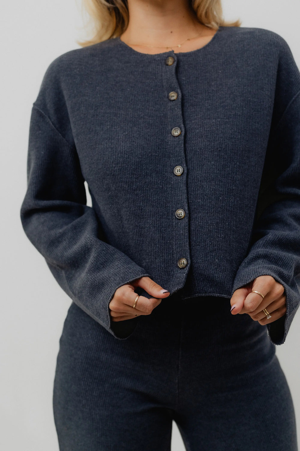 Person wearing a dark gray cardigan with button details on a plain background