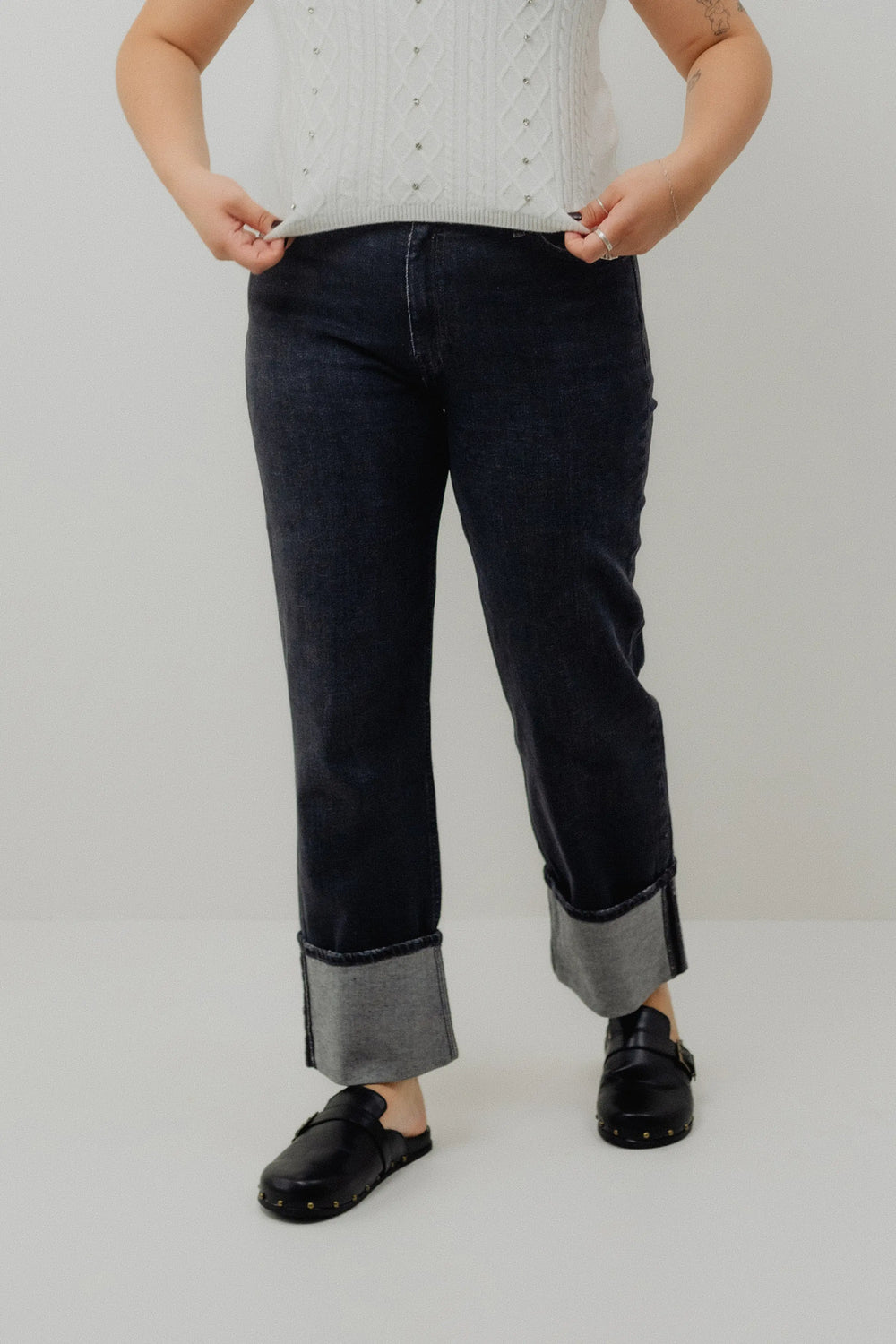 Person wearing black jeans with rolled-up cuffs on a plain background
