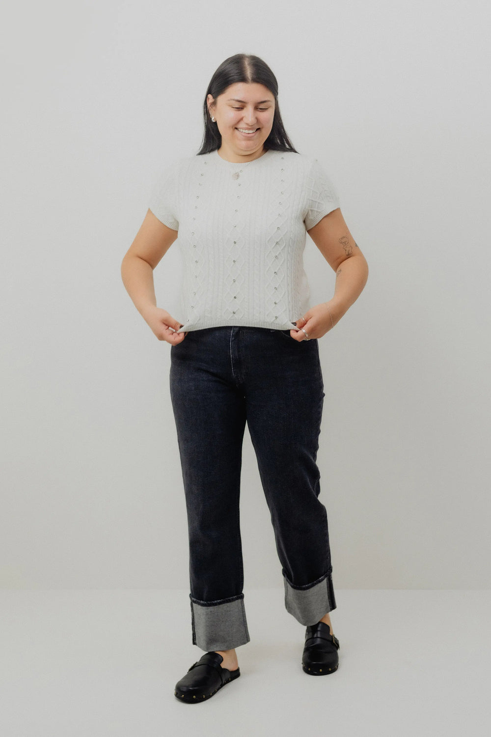 Woman wearing a light gray short-sleeve top and black jeans on a white background