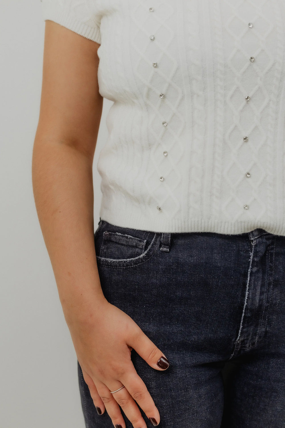 Woman wearing a light gray short-sleeve top and black jeans on a white background