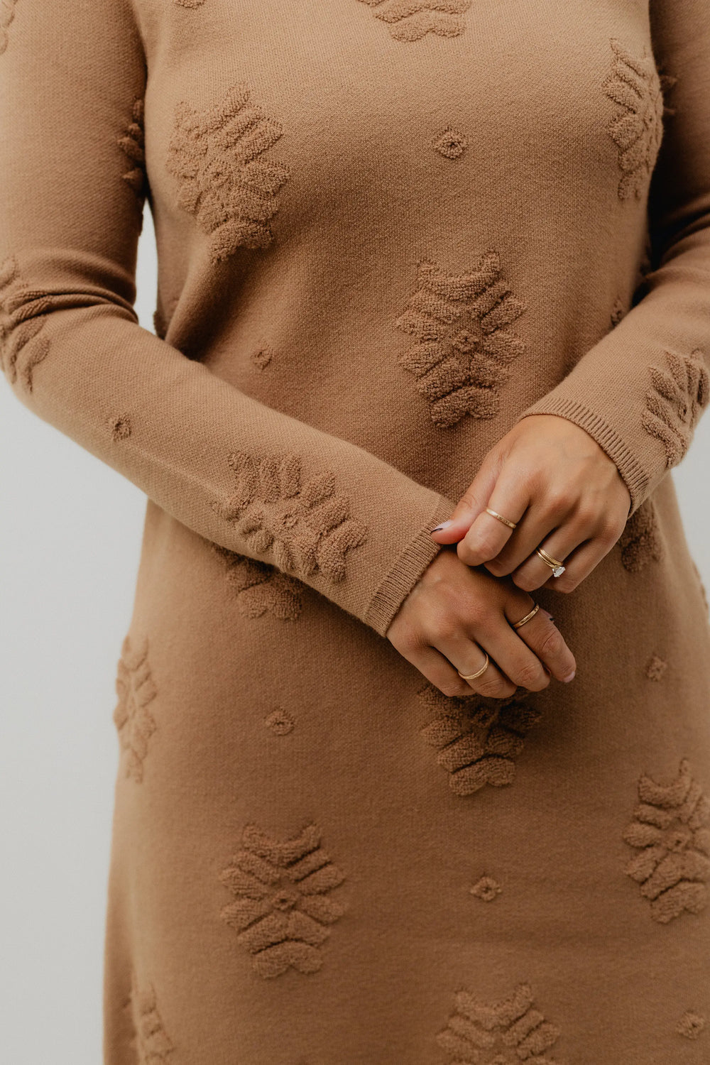 Woman wearing a brown dress with floral patterns and brown knee-high boots on a white background