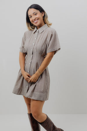 Woman wearing a striped shirt dress with brown boots on a plain background
