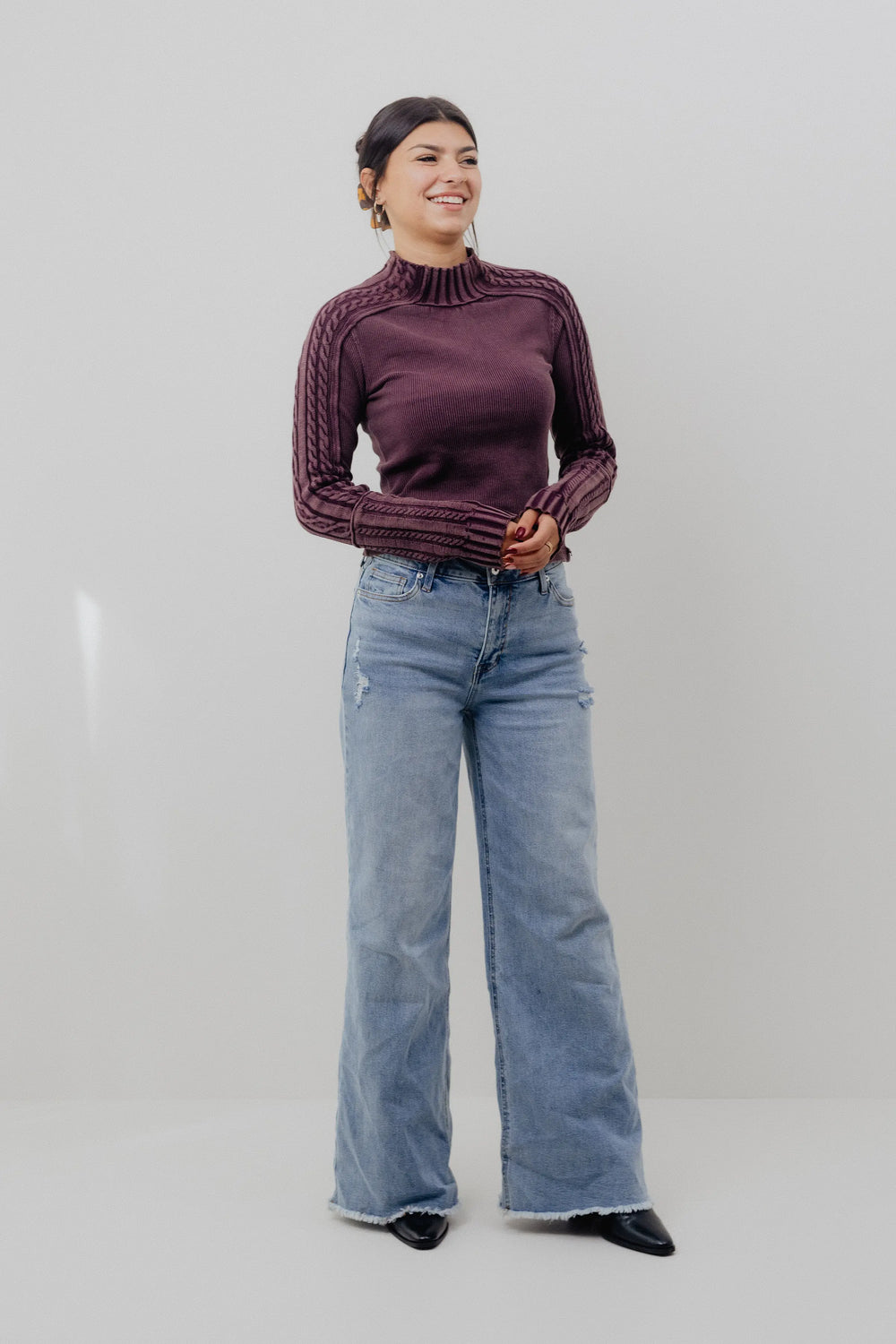 Woman wearing a maroon sweater and blue jeans against a white background