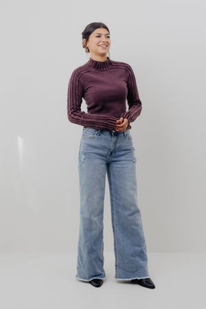 Woman wearing a maroon sweater and blue jeans against a white background