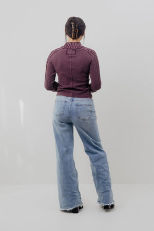 Person wearing a maroon jacket and light blue jeans on a plain background