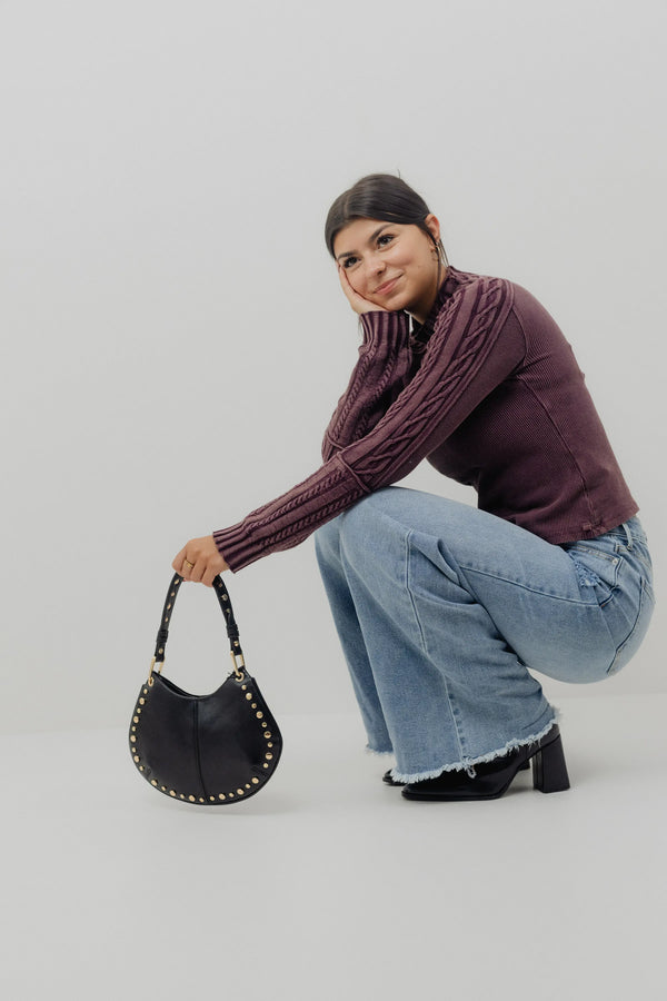 Woman holding a black handbag against a plain background
