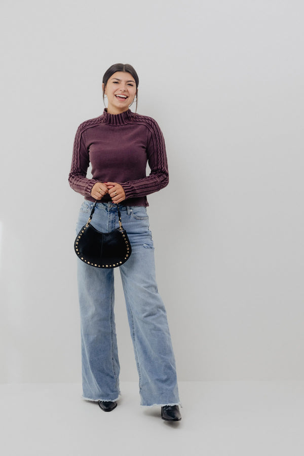 Person wearing a ribbed knit sweater and jeans, holding a black handbag on a plain background