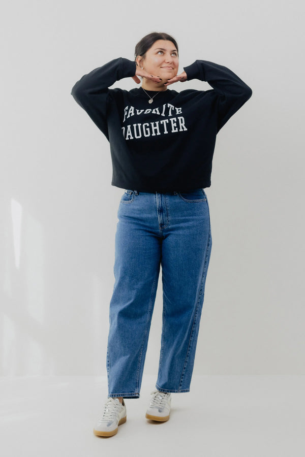 Person wearing a black sweatshirt with 'FAVORITE LAUGHTER' text and blue jeans on a light gray background