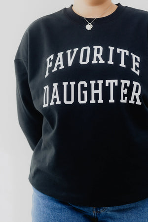 Black sweatshirt with 'FAVORITE DAUGHTER' text worn by a person on a plain background