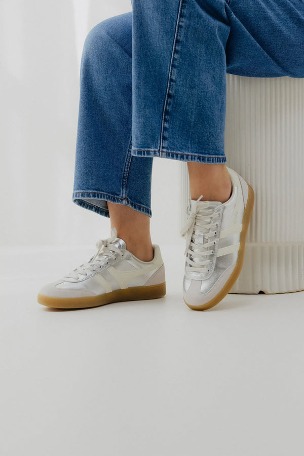White sneakers with brown soles worn with blue jeans on a white background
