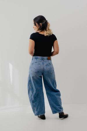Person wearing a black top and blue jeans on a plain background