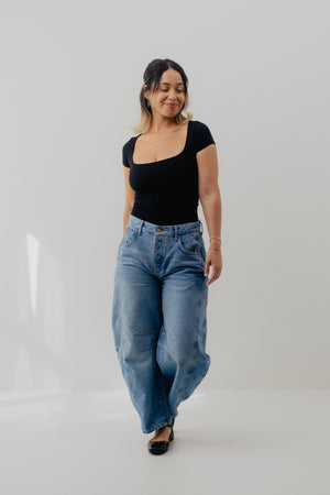 Woman wearing a black top and blue jeans on a white background