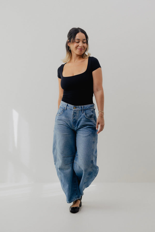Woman wearing a black top and blue jeans on a white background