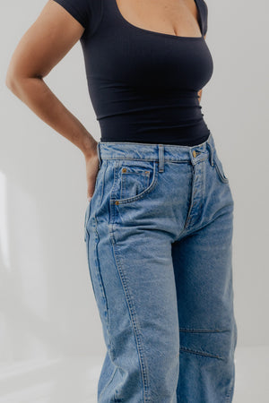 Person wearing a black top and blue jeans on a plain background