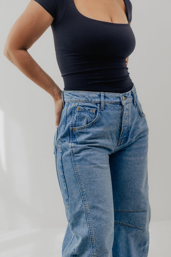 Person wearing a black top and blue jeans on a plain background