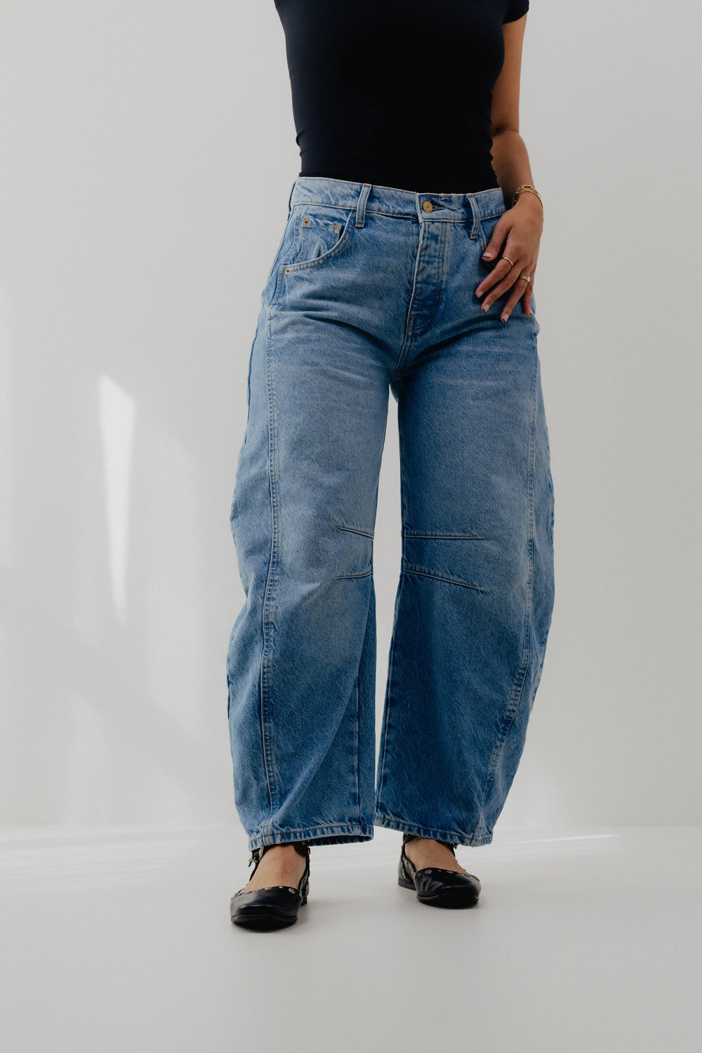Person wearing blue wide-leg jeans and black shoes on a white background