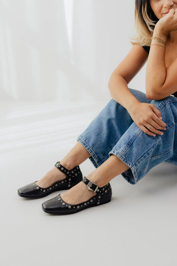 Person wearing black studded flats and blue jeans on a light background
