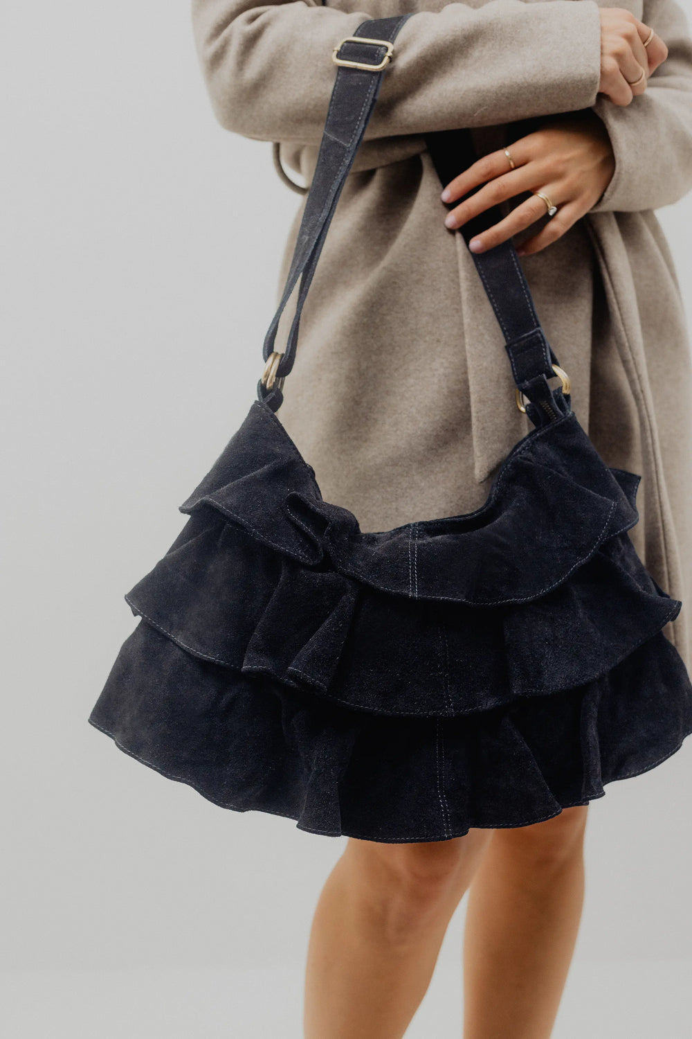 Person holding a dark blue ruffled handbag against a neutral background