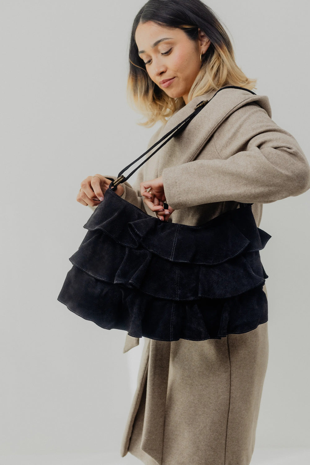 Person holding a dark blue ruffled handbag against a neutral background