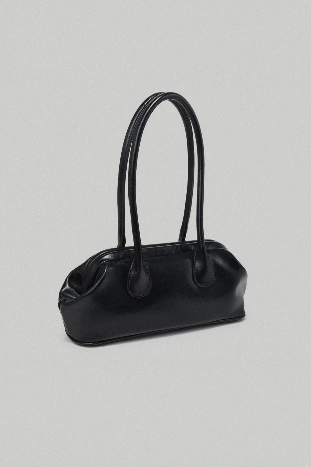 Person holding a black handbag with a plain background