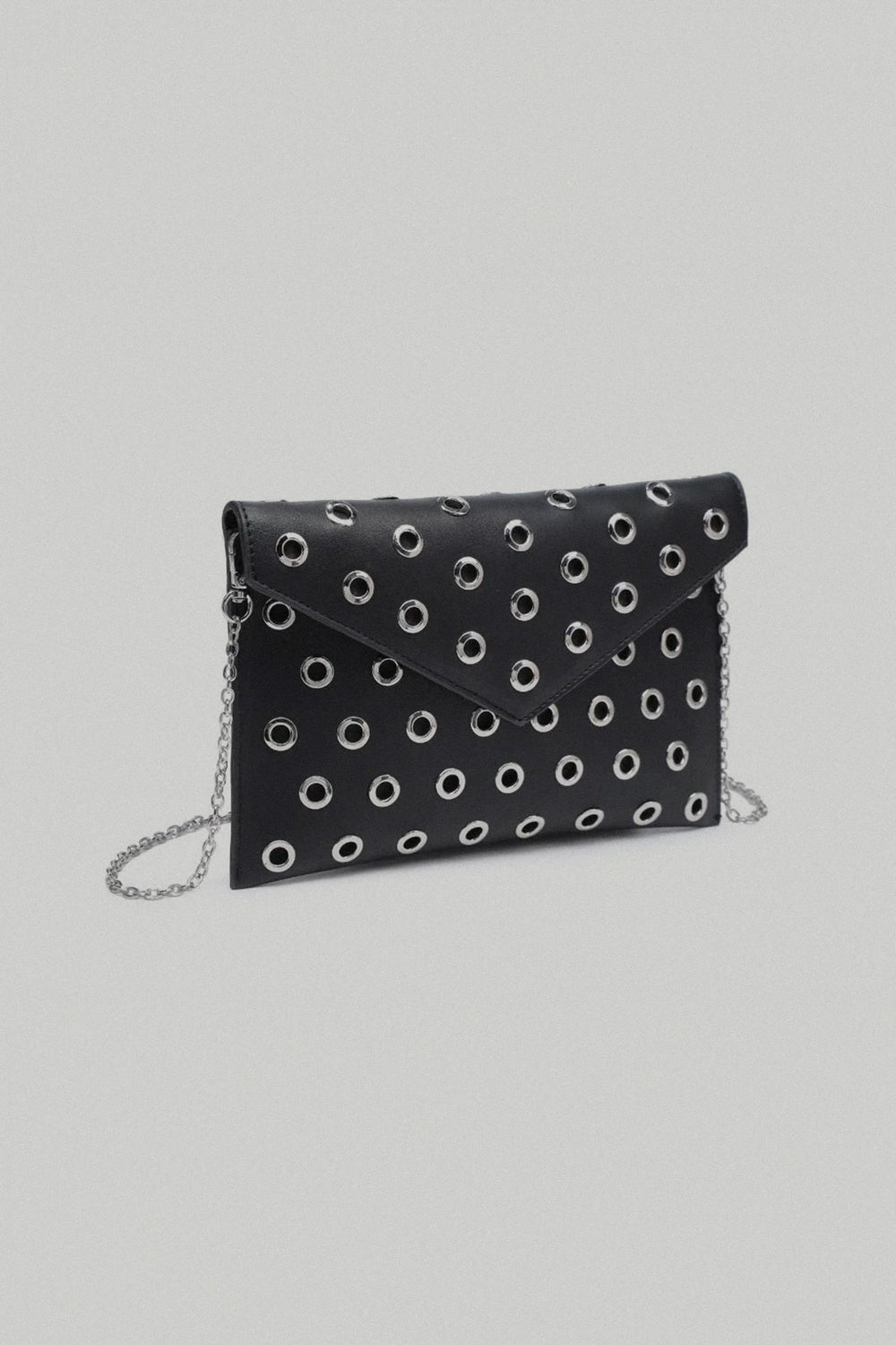 Black clutch bag with white polka dot pattern and chain strap on a light gray background