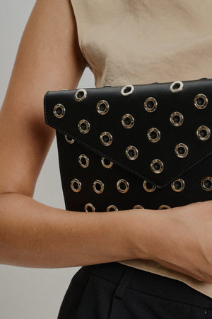Black clutch with gold studs held by a person against a neutral background